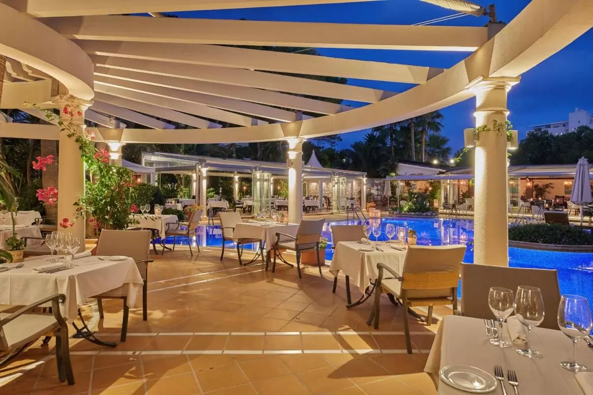 Área de comedor al aire libre junto a piscina iluminada en ambiente nocturno con estructura de vigas blancas en Mallorca