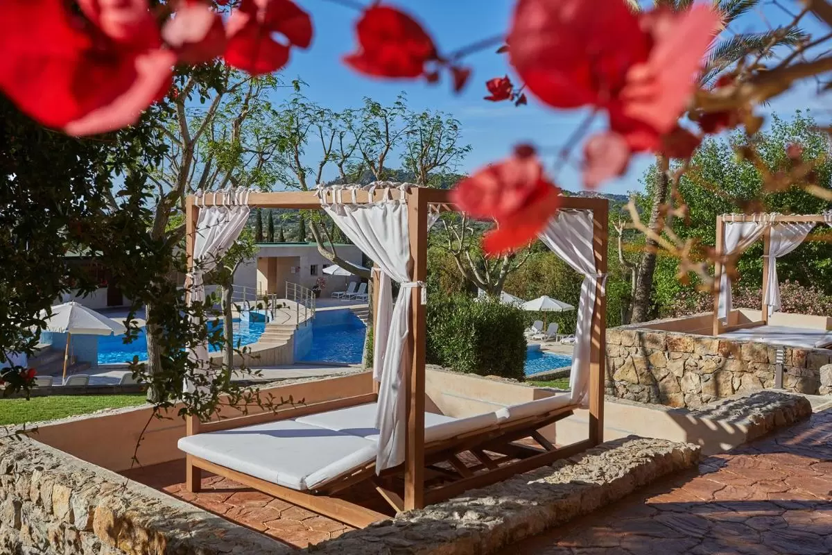Área de descanso junto a piscina con estructura de madera, cortinas blancas y tumbonas en Mallorca