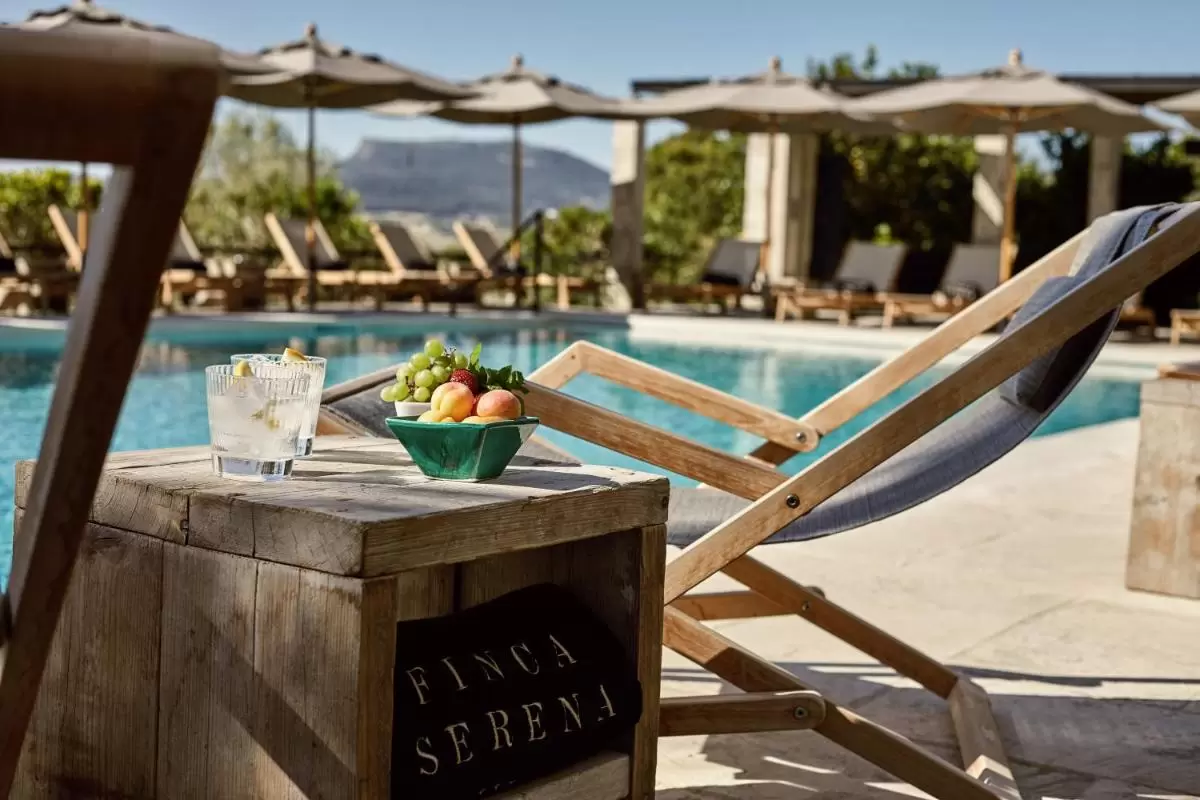 Finca Serena Mallorca, Small Luxury Hotels Área de piscina al aire libre en Mallorca con mesa rústica, bebidas frescas y tumbonas bajo sombrillas claras