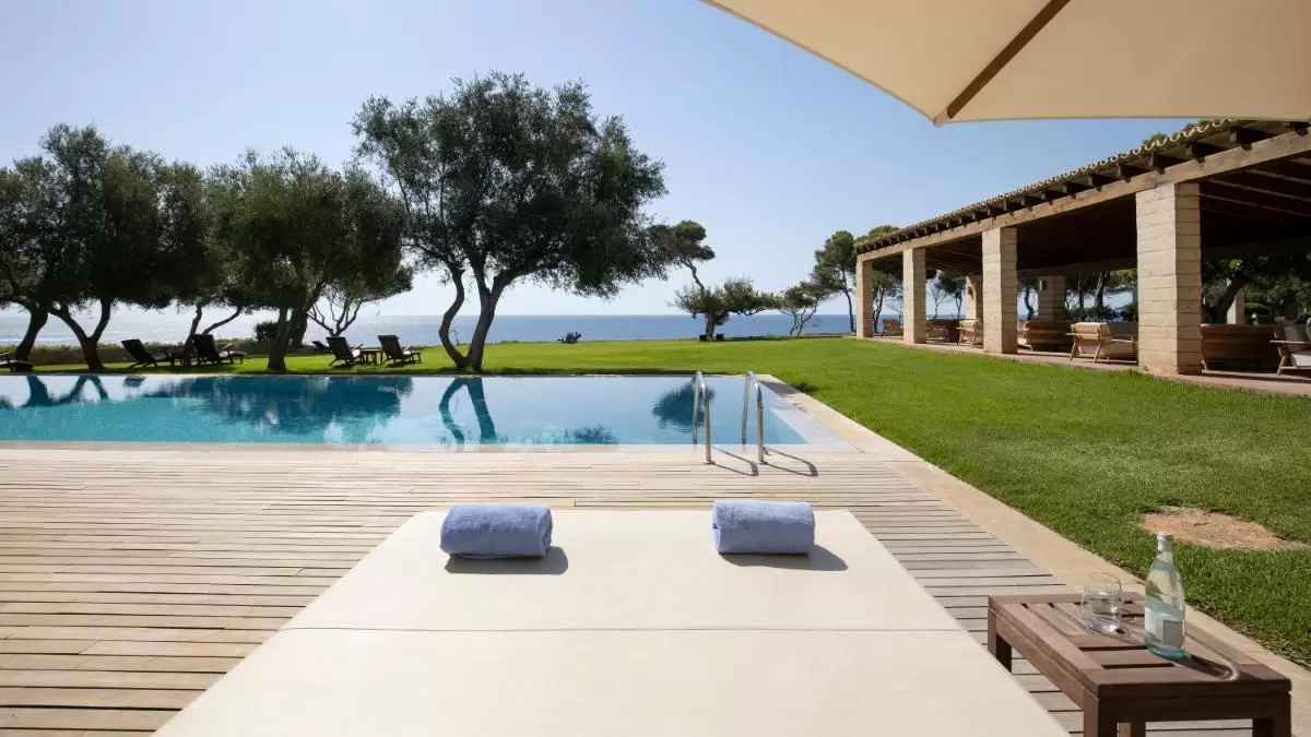 Área exterior con piscina de borde infinito, deck de madera y espacio de descanso frente al mar en Mallorca