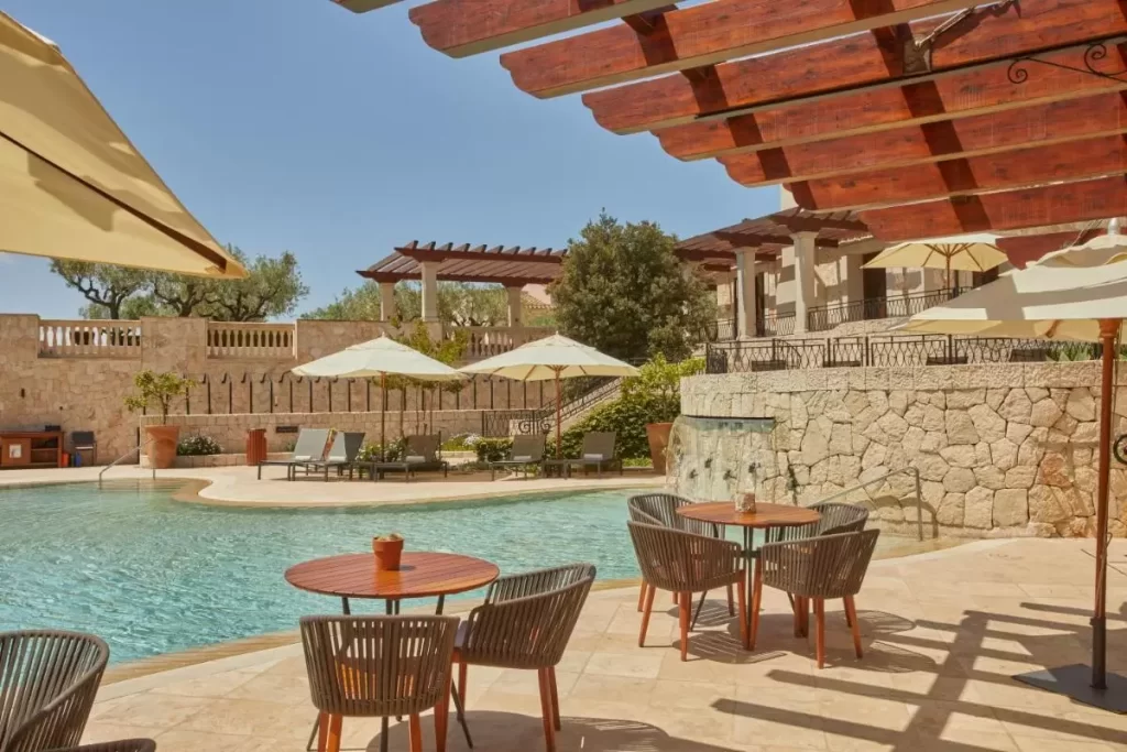 Área exterior con piscina irregular, pérgola de madera, tumbonas con parasoles y decoración natural en Mallorca