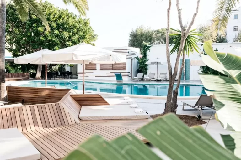 Área exterior con piscina rectangular, deck de madera, tumbonas con cojines y sombrillas blancas en Mallorca
