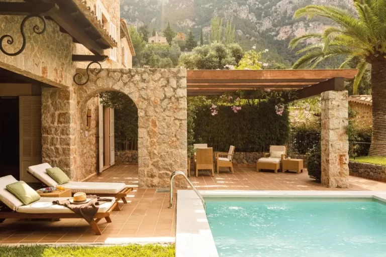 Área exterior con piscina rectangular, pérgola de madera y muebles de mimbre en entorno natural de Mallorca