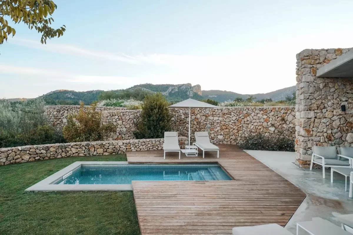 Área exterior con piscina rectangular, plataforma de madera, tumbonas y muro de piedra en Mallorca