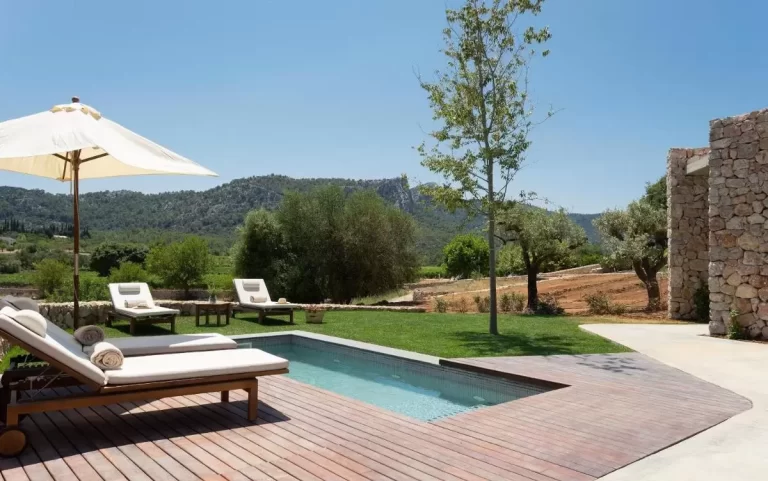 Área exterior con piscina rectangular, tumbonas con cojines blancos y plataforma de madera en Mallorca
