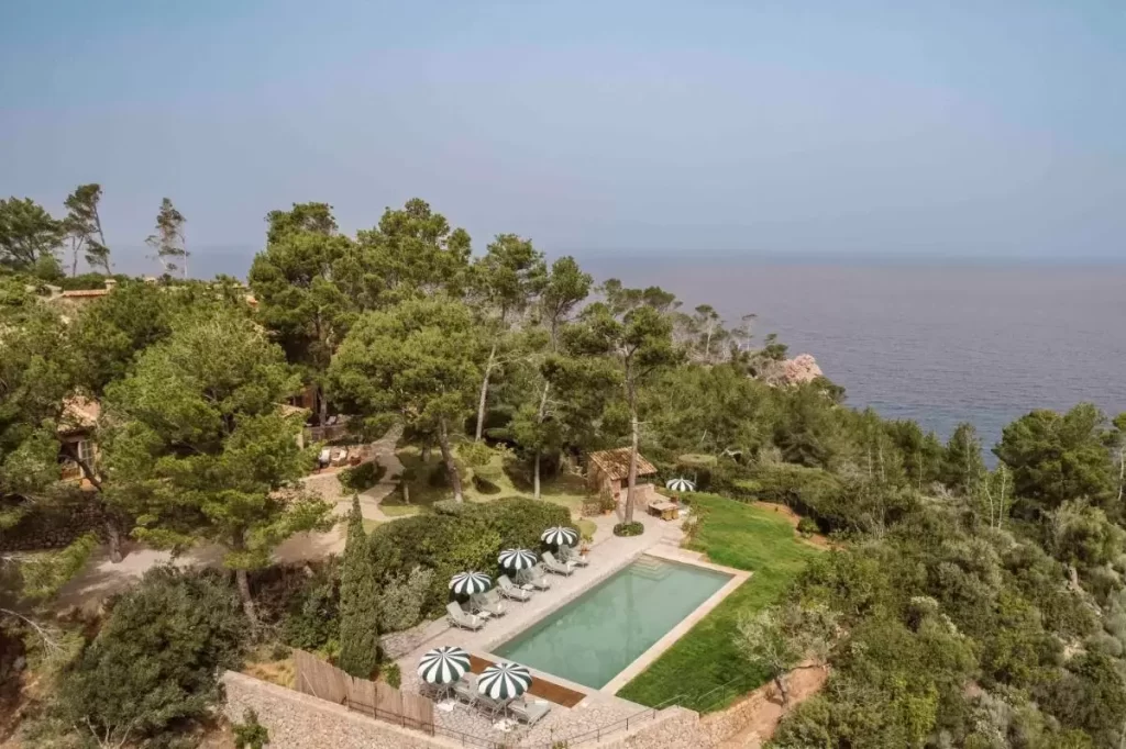 Área exterior con piscina rectangular, tumbonas con sombrillas, jardín y vista panorámica al mar en Mallorca