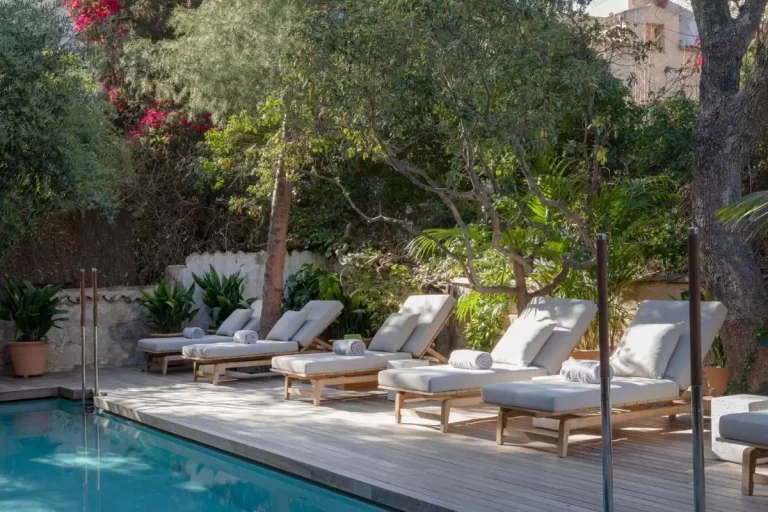 Área exterior con piscina rectangular y deck de madera clara con tumbonas reclinables en Mallorca