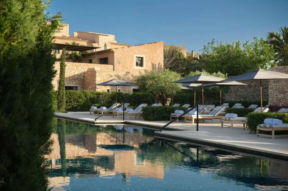 Área exterior con piscina rectangular y deck de piedra rodeada de tumbonas y vegetación mediterránea en Mallorca