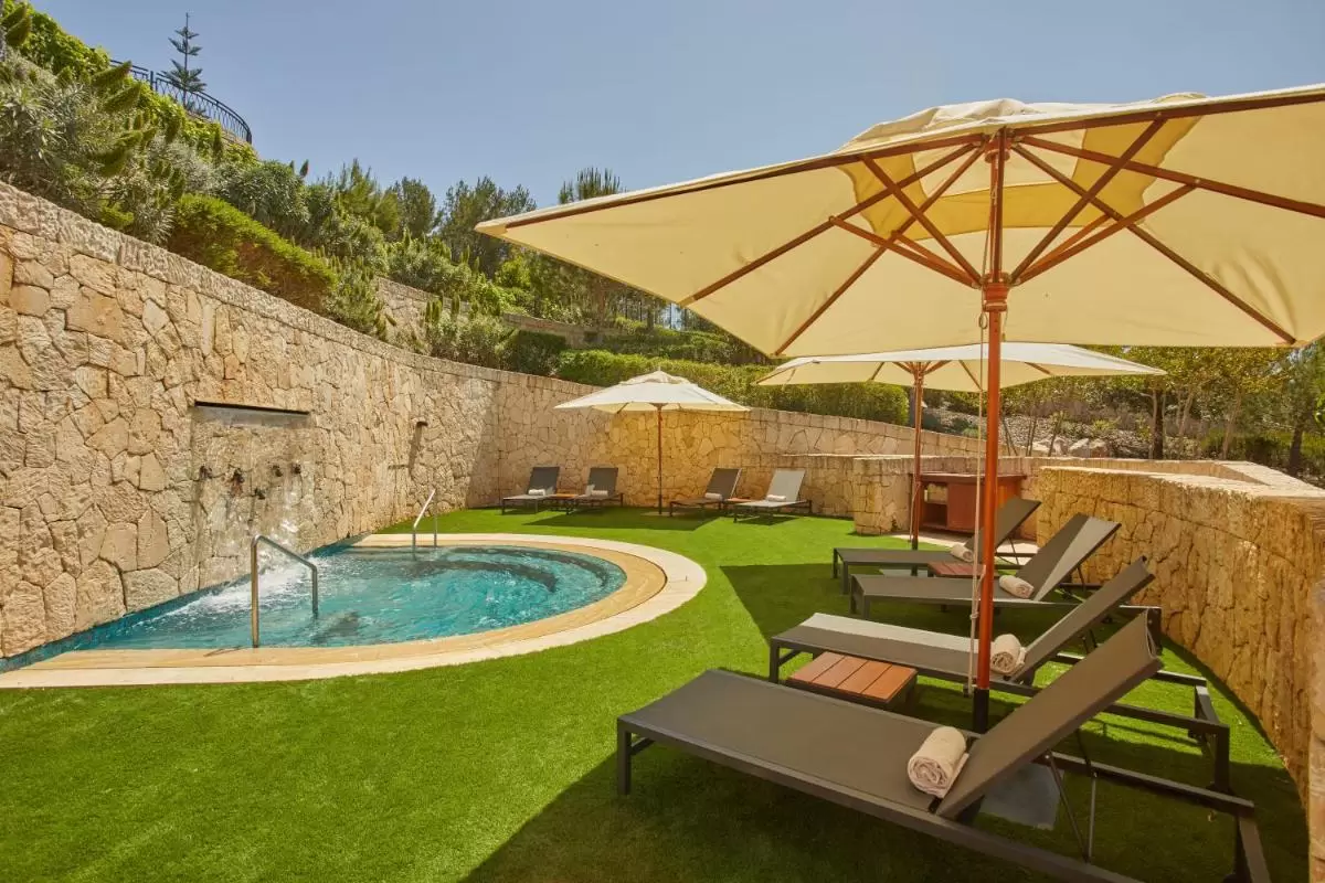 Área exterior de descanso con tumbonas, sombrillas y piscina ovalada con cascada en Mallorca