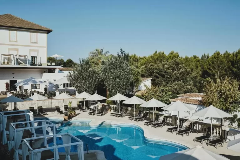 Área exterior de piscina irregular con tumbonas, sombrillas y cabañas en terraza pavimentada en Mallorca