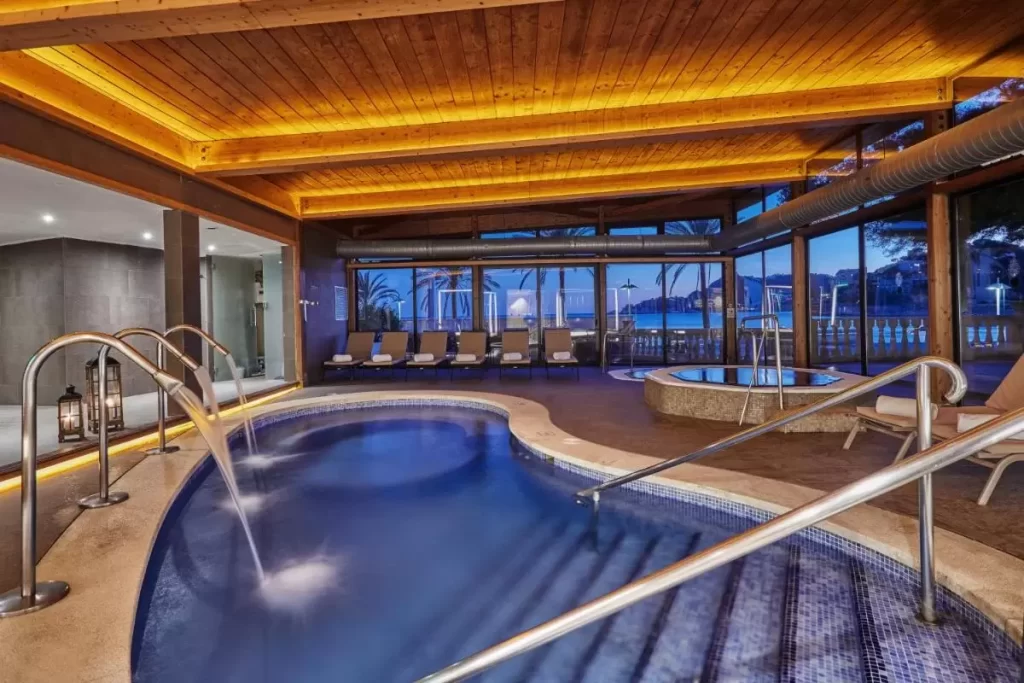 Área interior de piscina y jacuzzi con diseño orgánico, iluminación cálida y vistas panorámicas en Mallorca