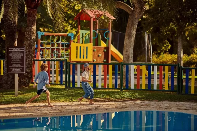 Área recreativa al aire libre en Mallorca con piscina, parque infantil colorido y sendero pavimentado para niños