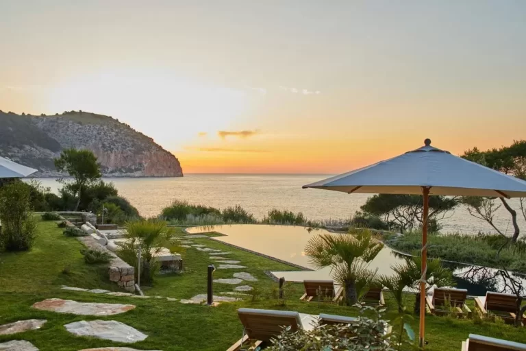 Atardecer en Mallorca con piscina de borde infinito, jardín cuidado y vistas al mar tranquilo desde acantilado rocoso