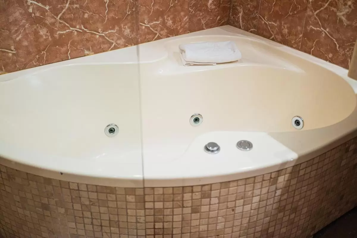 Bañera de esquina blanca con jets de hidromasaje y revestimiento de azulejos beige y marrón en Mallorca