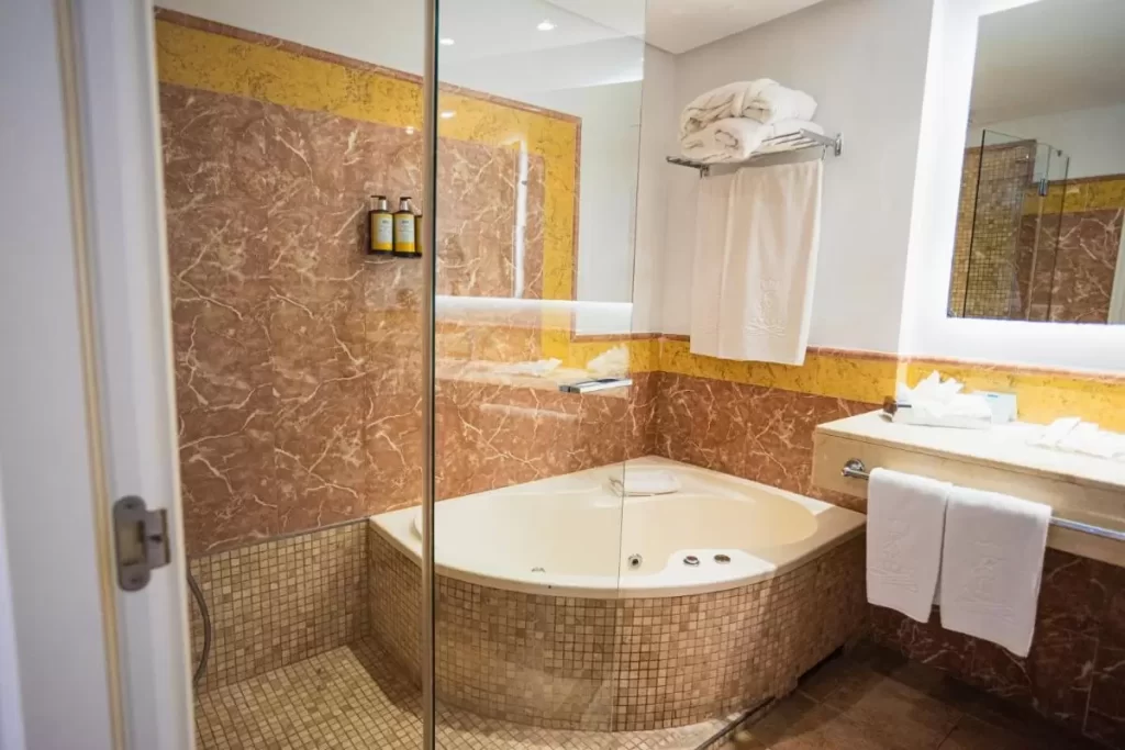 Baño con bañera de esquina con jets de hidromasaje y revestimientos en tonos beige y marrón en Mallorca