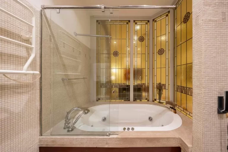 Baño con bañera ovalada de hidromasaje y mampara de vidrio templado en tonos beige cálidos en Mallorca