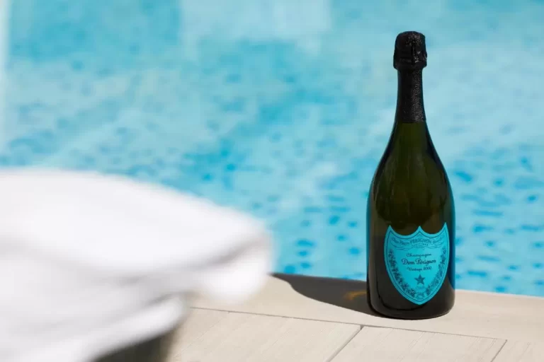 Botella de vidrio oscuro sobre borde de piscina con agua azul y toalla blanca en Mallorca