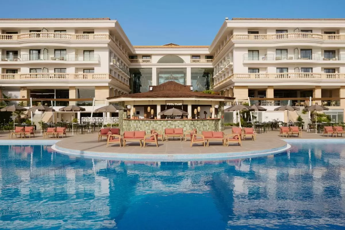 Complejo con piscina amplia y bar de techo de paja en terraza con mobiliario coral y sombrillas grises en Mallorca