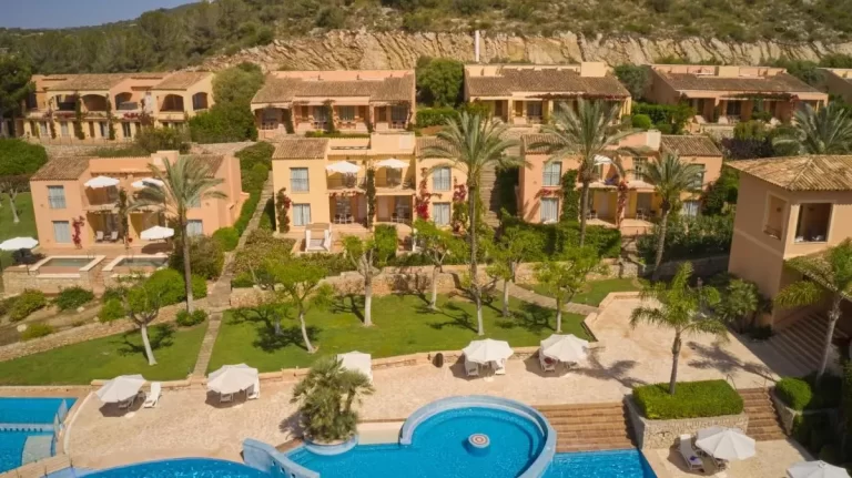 Conjunto residencial en Mallorca con piscina irregular, terrazas, jardines y palmeras en entorno natural