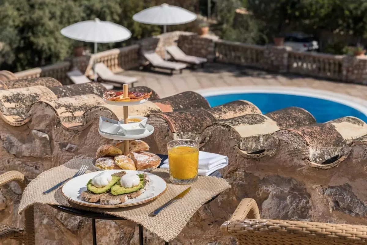 Desayuno al aire libre junto a piscina ovalada con tumbonas y sombrillas en terraza soleada de Mallorca