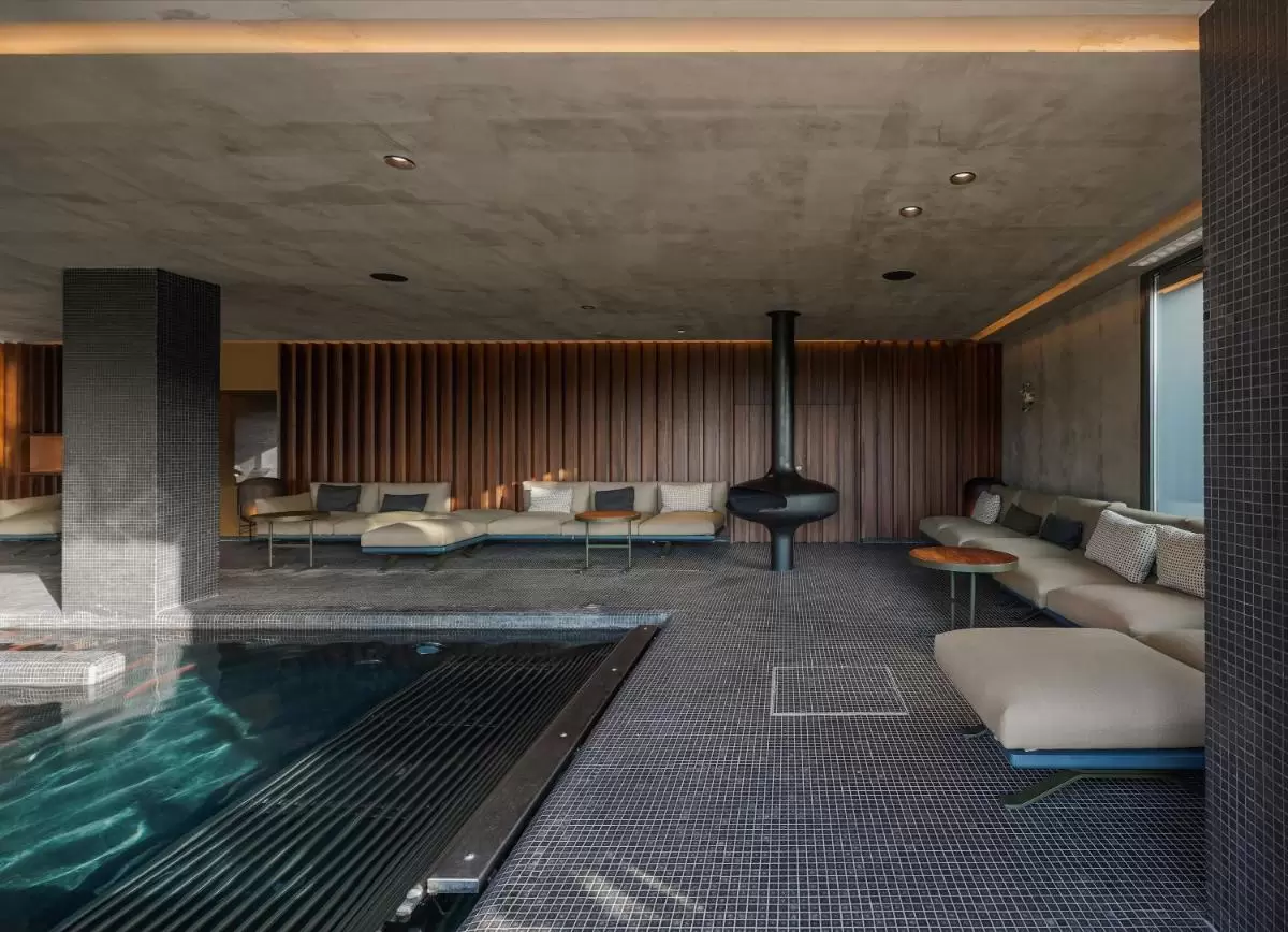 Diseño contemporáneo de piscina cubierta con chimenea suspendida y revestimientos en madera y baldosas oscuras en Mallorca