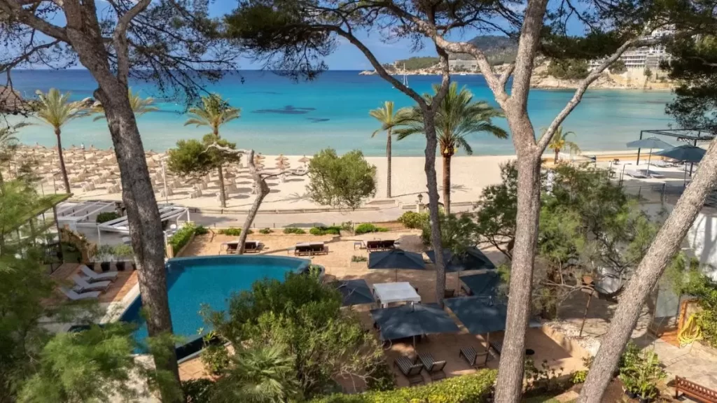 Escena costera en Mallorca con piscina irregular, playa de arena clara y mar turquesa transparente