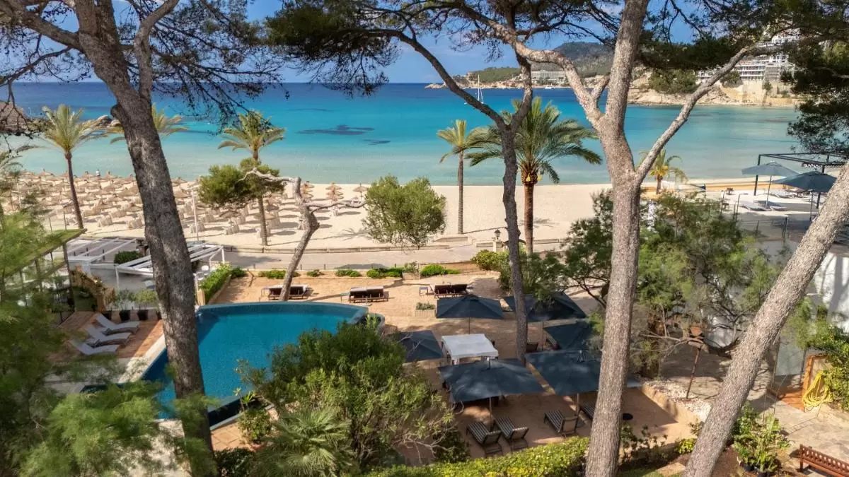 Escena costera en Mallorca con piscina irregular, playa de arena clara y mar turquesa transparente