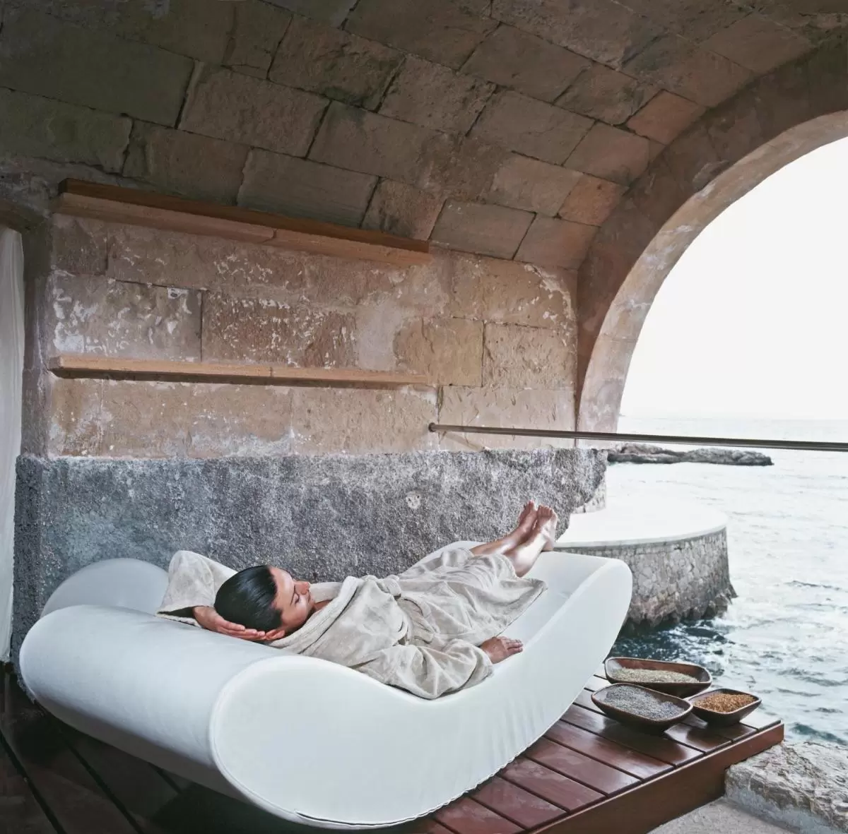 Espacio de relajación con camilla curva y vista al mar en entorno de piedra natural en Mallorca