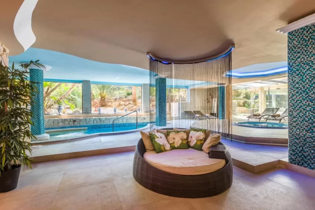 Espacio interior de spa en Mallorca con piscina cubierta, sillón de mimbre y zona de tumbonas reclinables
