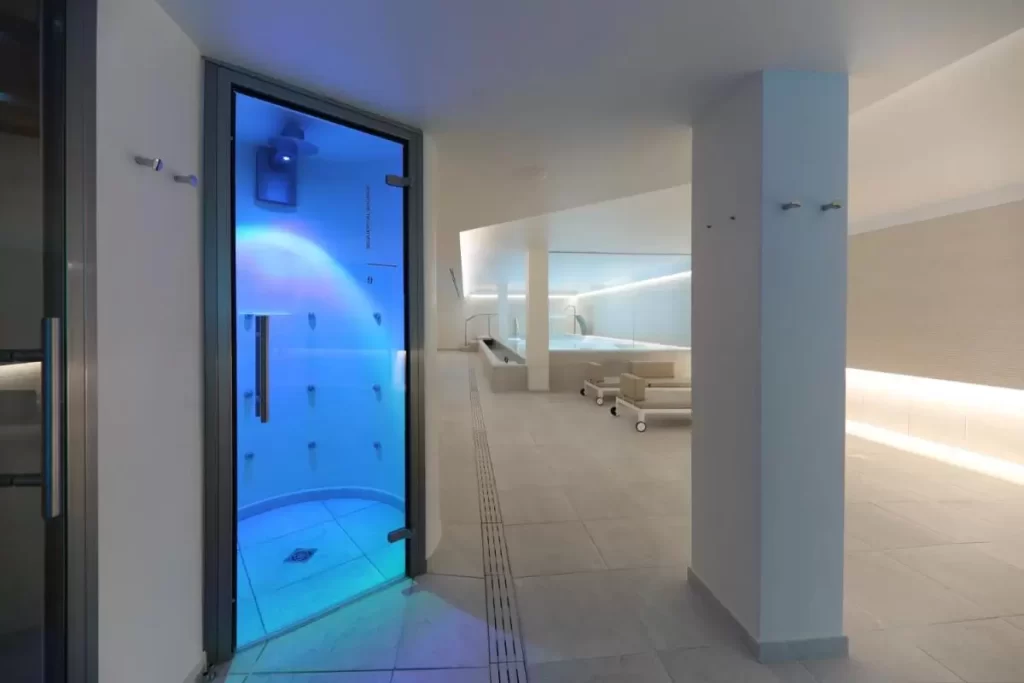 Espacio interior moderno con ducha de luz azul, piscina elevada y camastros en Mallorca