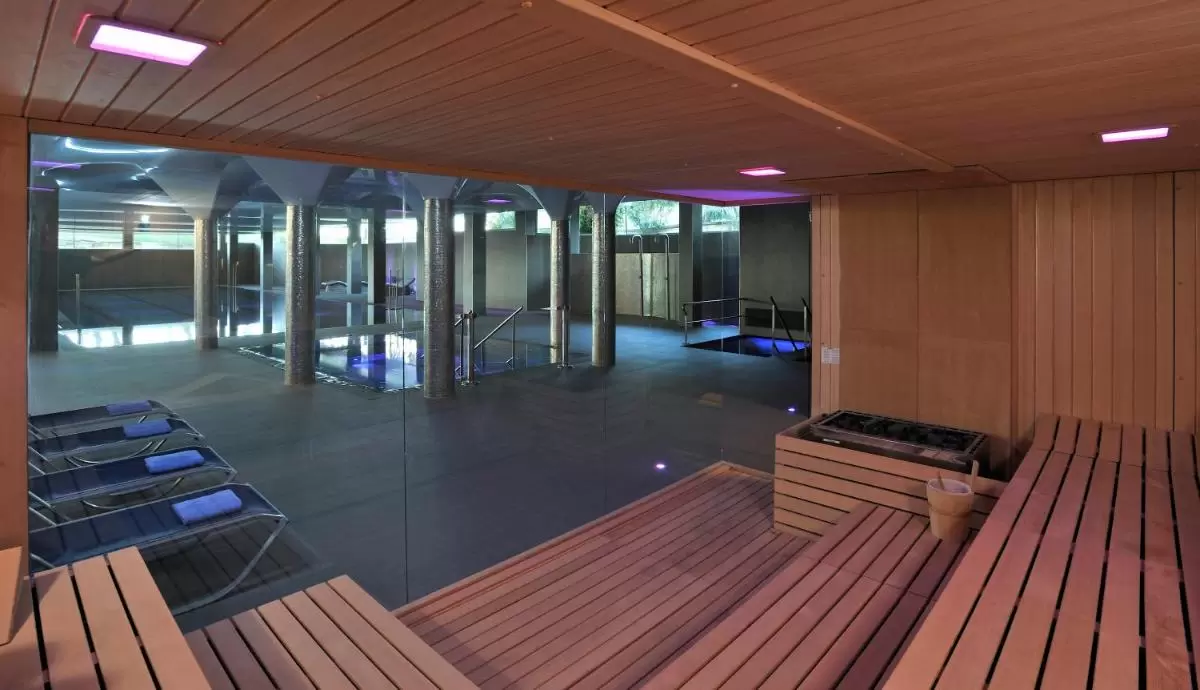 Iberostar Selection Playa de Muro Village Espacio interior moderno con sauna de madera y piscina cubierta con iluminación púrpura en Mallorca