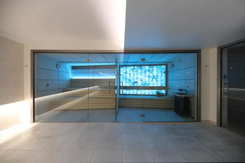 Espacio interior moderno con sauna de vidrio, bancos de madera y luz azul en Mallorca