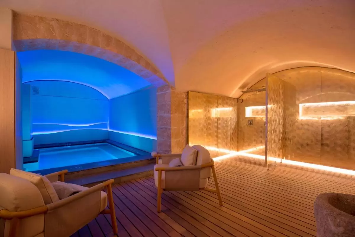 Espacio interior moderno y cálido con piscina iluminada en azul y zona de ducha metálica en Mallorca