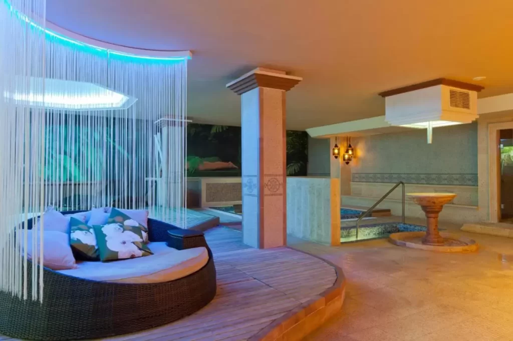 Espacio interior relajante con jacuzzi, asiento circular de mimbre, iluminación azul y decoración natural en Mallorca