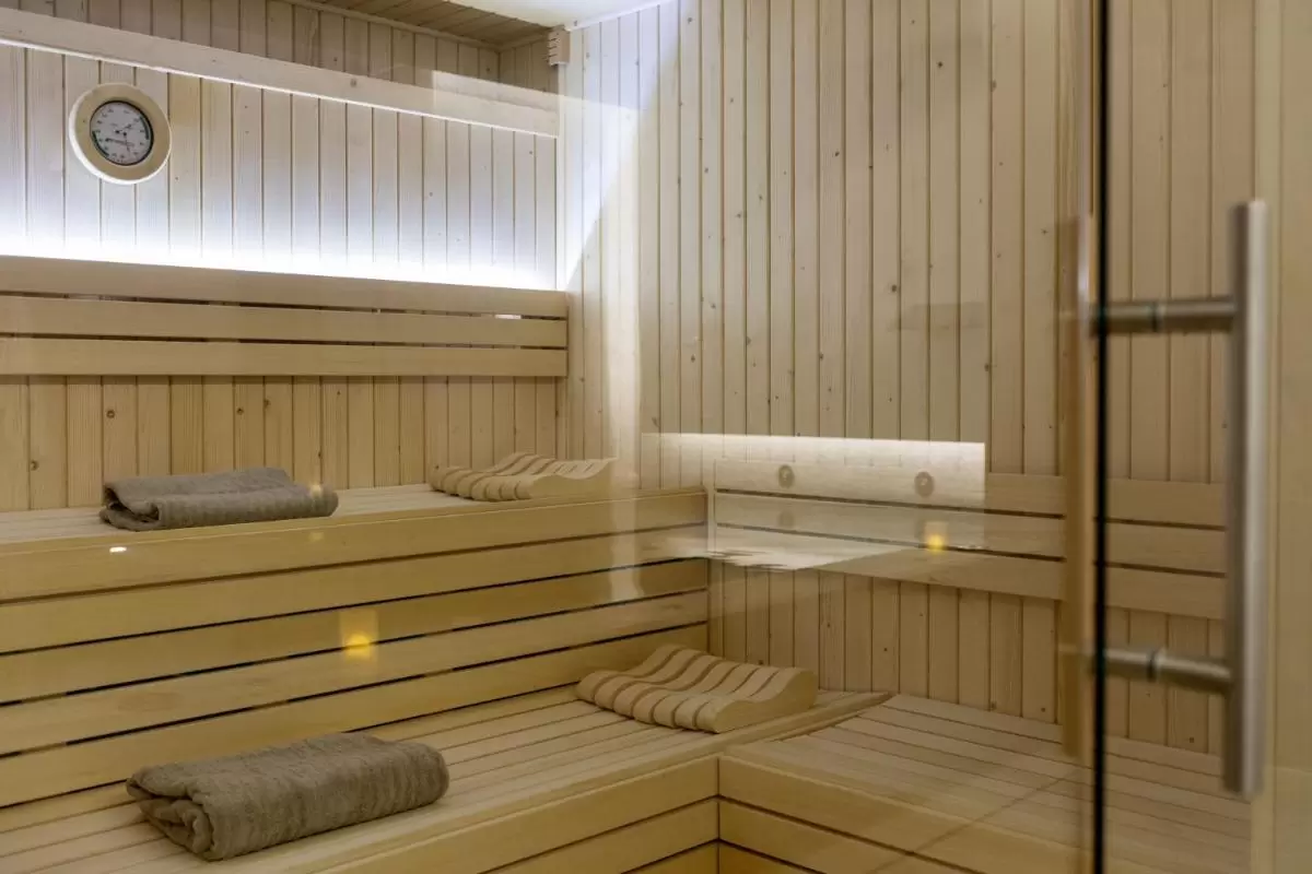 Interior de sauna de madera clara con bancos en L, iluminación indirecta y termómetro en Mallorca