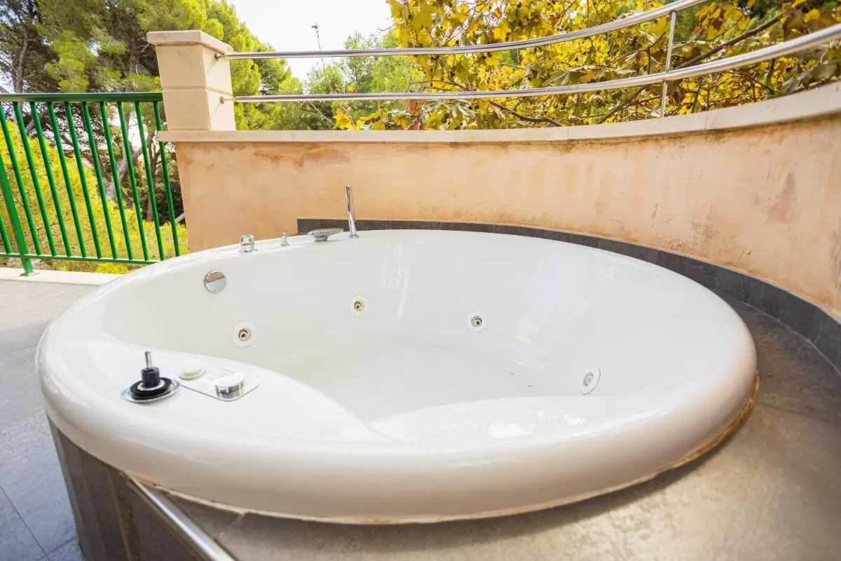 Jacuzzi circular empotrado en terraza con barandilla verde y entorno natural en Mallorca