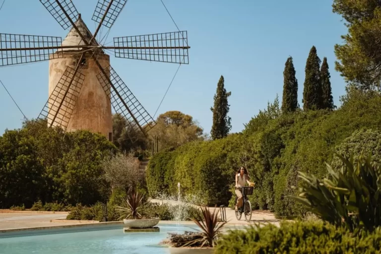 Paisaje exterior en Mallorca con molino tradicional, fuente decorativa y camino rodeado de setos verdes para relajación