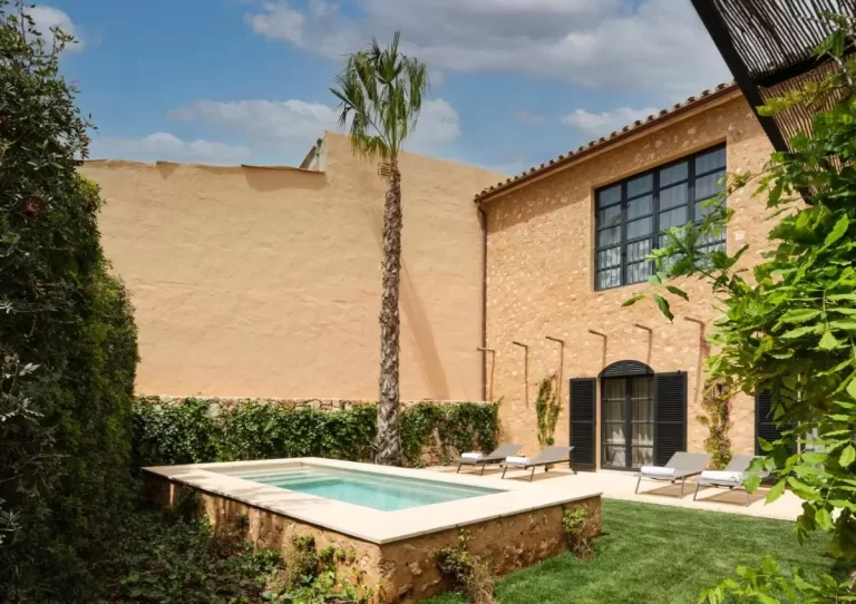 Patio exterior en Mallorca con piscina elevada de piedra rústica y área de descanso con tumbonas y palmera