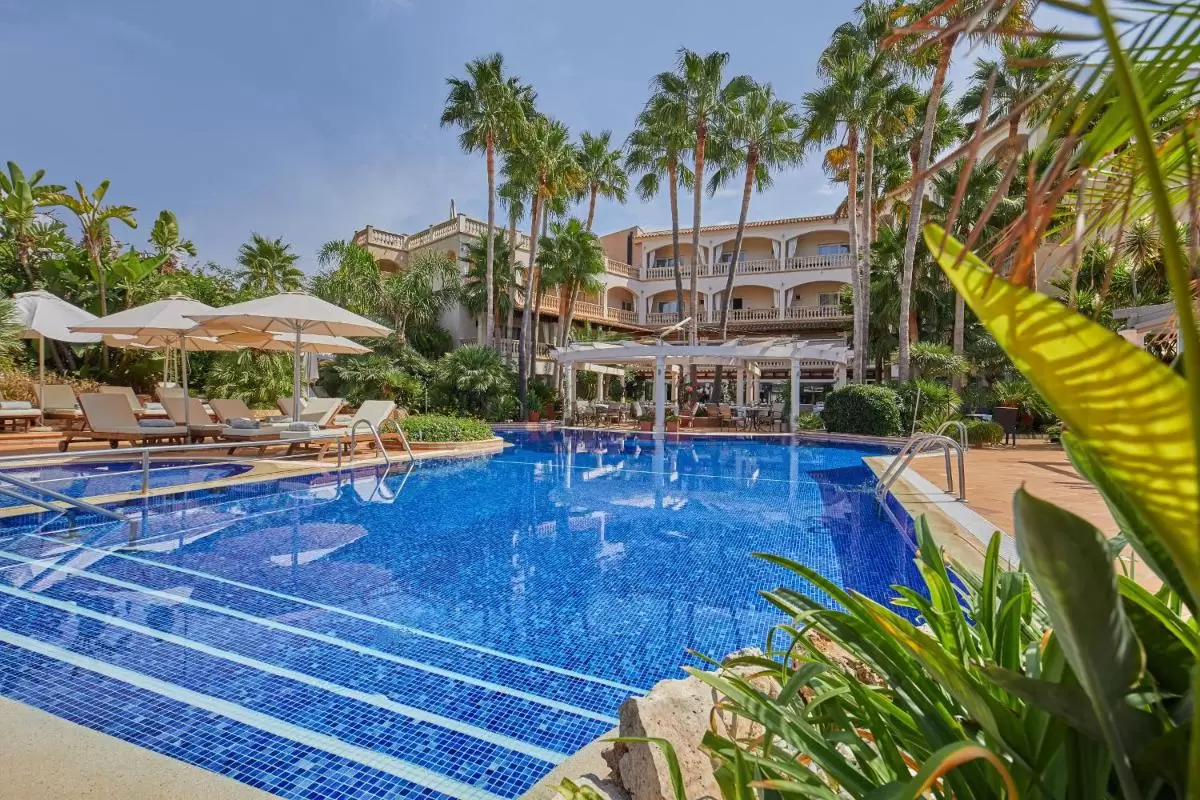 Piscina al aire libre con azulejos azules, tumbonas, pérgola y vegetación tropical en Mallorca