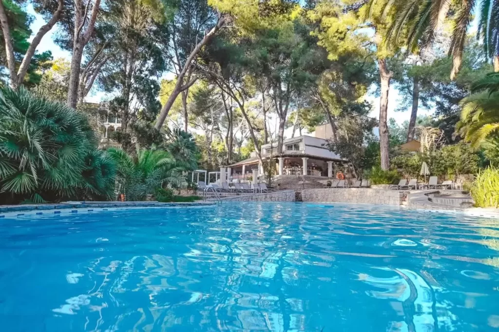 Lago Garden Apart-Suites & Spa Hotel Piscina al aire libre con bordes de piedra y terraza cubierta rodeada de vegetación en Mallorca