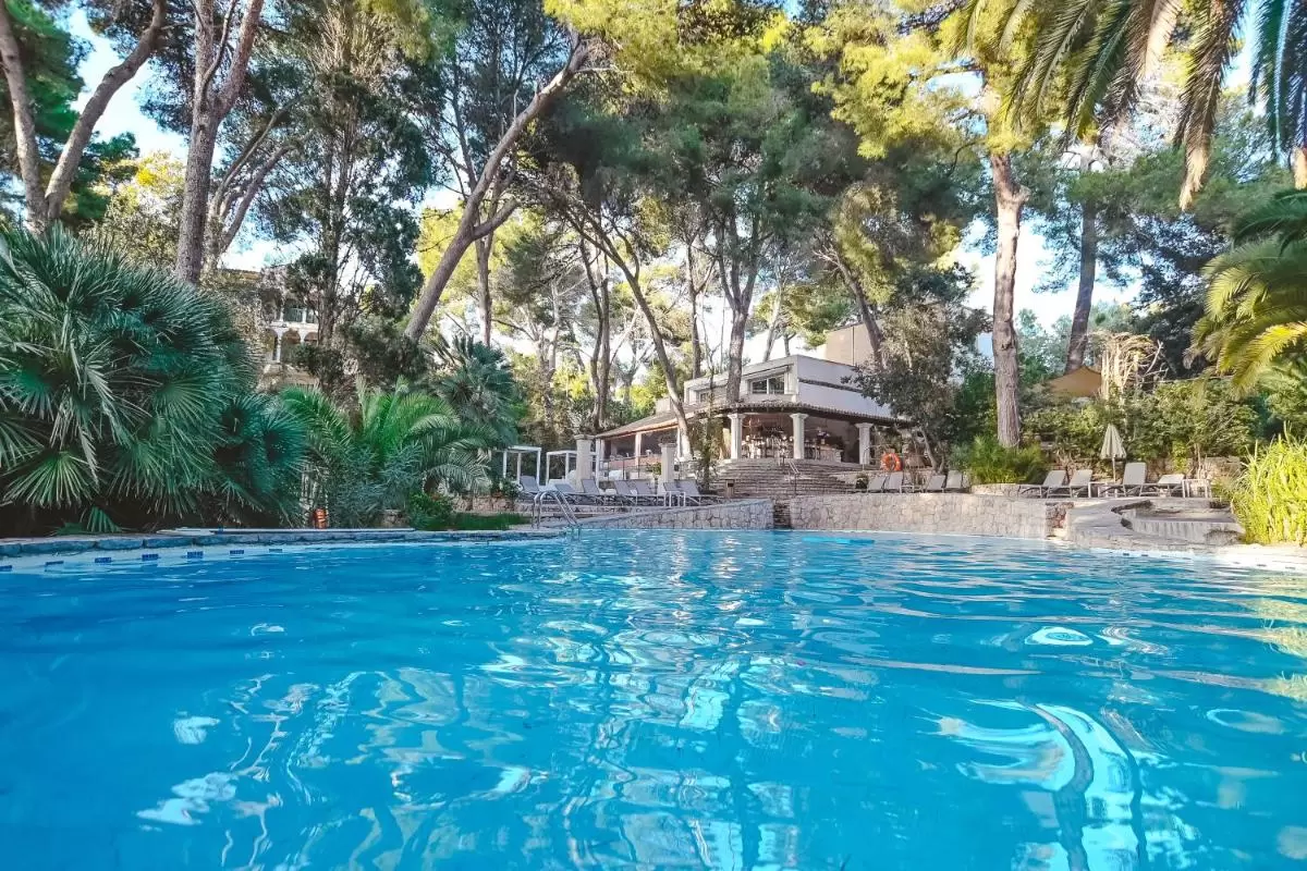 Piscina al aire libre con bordes de piedra y terraza cubierta rodeada de vegetación en Mallorca