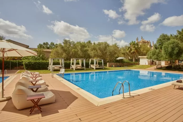 Piscina al aire libre con deck de madera, camas balinesas y entorno natural en Mallorca soleada