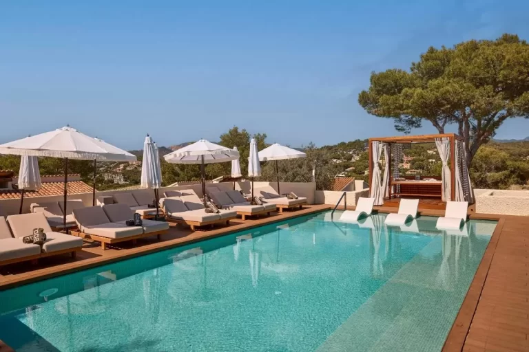 Piscina al aire libre con deck de madera, tumbonas beige y reposeras blancas parcialmente sumergidas en Mallorca