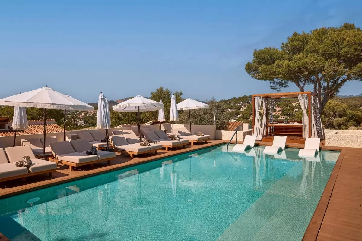 Piscina al aire libre con deck de madera, tumbonas beige y reposeras blancas parcialmente sumergidas en Mallorca