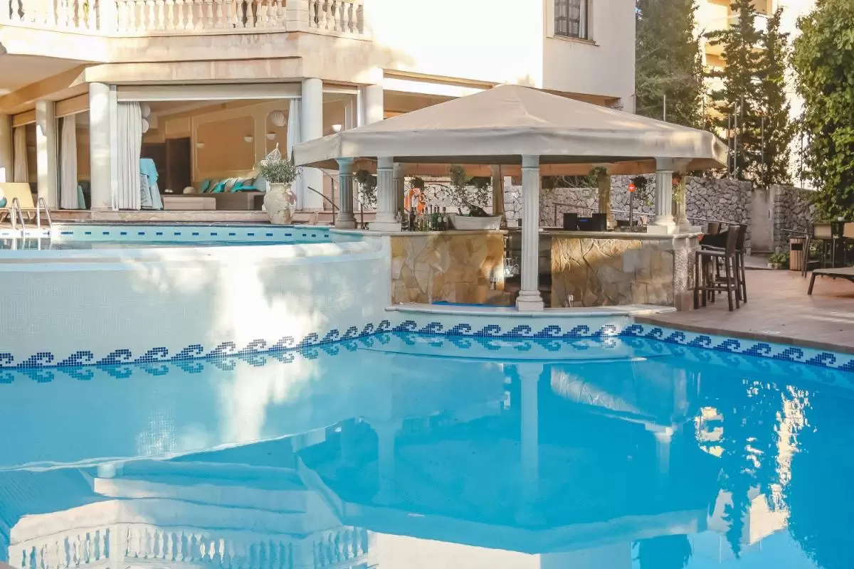 Piscina al aire libre con diseño curvo, azulejos decorativos y área de bar con toldo en Mallorca