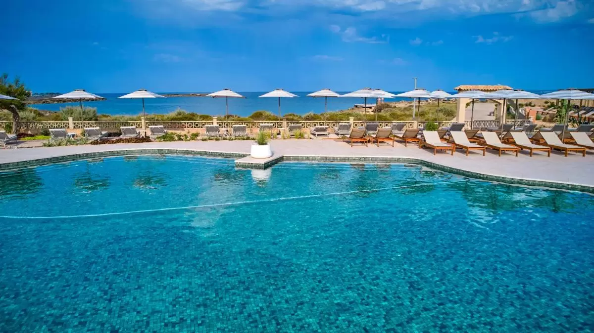 Piscina al aire libre con diseño de mosaico, tumbonas con sombrillas y vistas al mar en Mallorca
