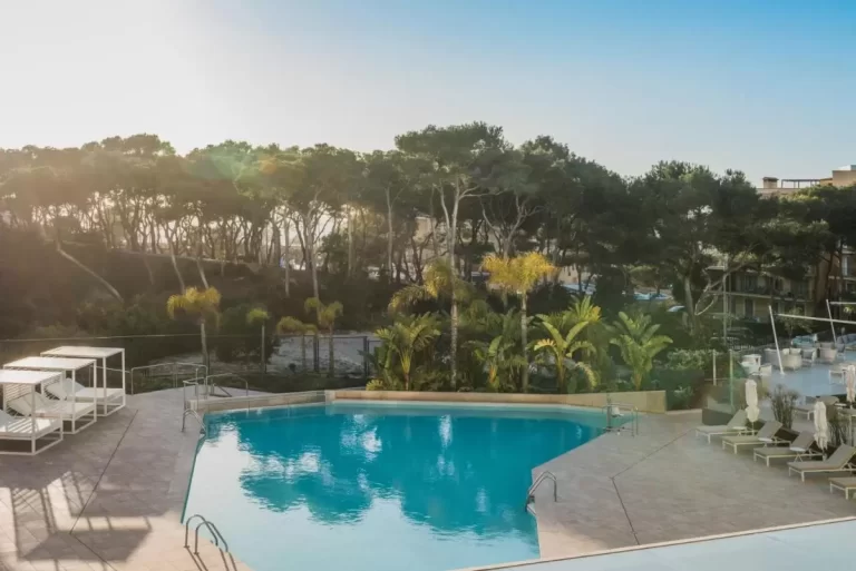 Piscina al aire libre con diseño irregular, camas de descanso y tumbonas en entorno ajardinado en Mallorca