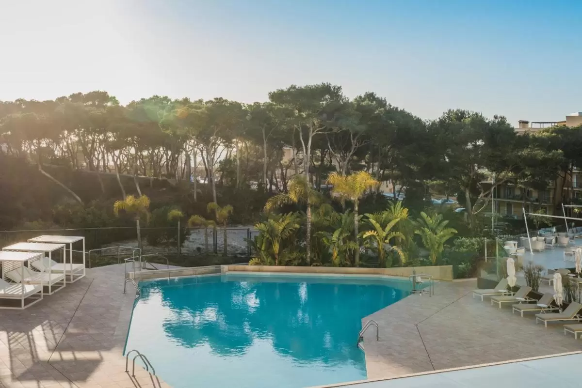 Piscina al aire libre con diseño irregular, camas de descanso y tumbonas en entorno ajardinado en Mallorca