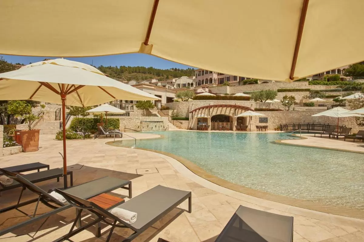 Piscina al aire libre con diseño irregular, tumbonas grises y sombrillas beige en entorno mediterráneo en Mallorca
