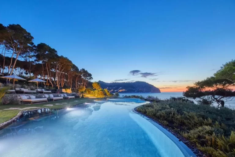 Piscina al aire libre con diseño natural e iluminación ambiental junto al mar en Mallorca al atardecer